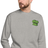 A model wearing a light grey crewneck sweatshirt with the Woodland Alliance meeple embroidered on the left chest. 
