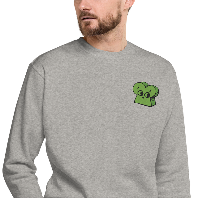 A model wearing a light grey crewneck sweatshirt with the Woodland Alliance meeple embroidered on the left chest. 
