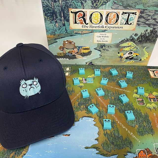 Our Riverfolk cap, featuring the Otter's VP marker embroidery, next to the Riverfolk expansion and meeples