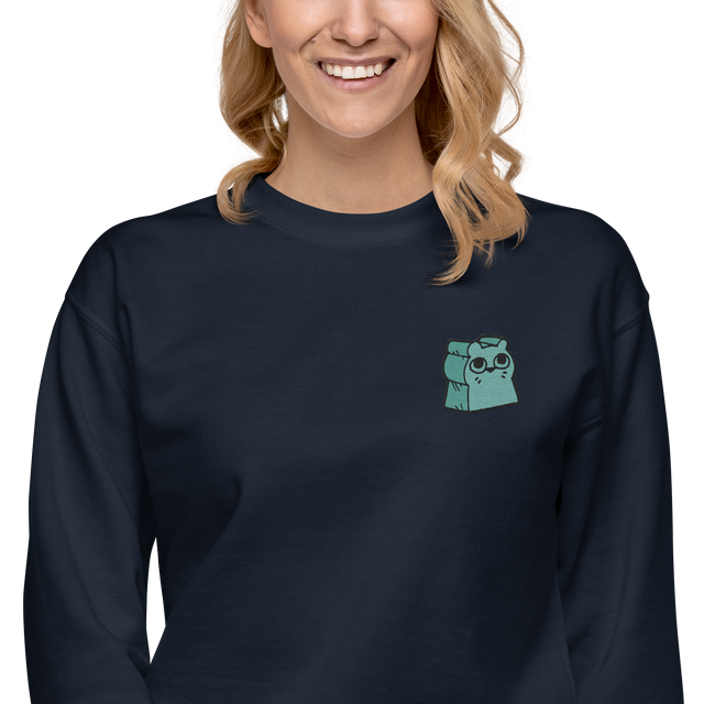 Model wearing a navy crewneck sweatshirt with the Riverfolk Otter meeple embroidered on the left chest. 