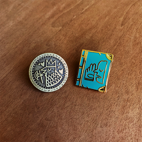 A photo of the two enamel pins on a wooden table